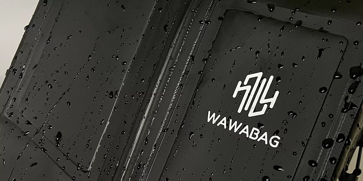 黑色 PVC Wawabag 的特寫，表面有雨滴，精美地突出了品牌標誌。.